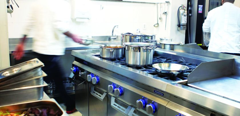 Professional kitchen with cooks handling sauce pans. 